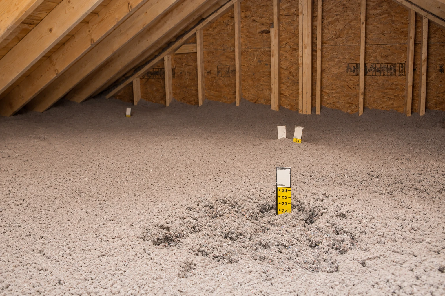 An unfinished attic floor blanketed in loose-fill insulation, with depth markers standing above the fill.