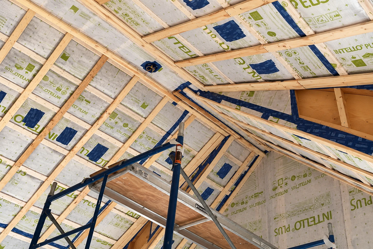 Vapor barrier sheeting covers the underside of an attic roof, held between exposed wooden rafters.